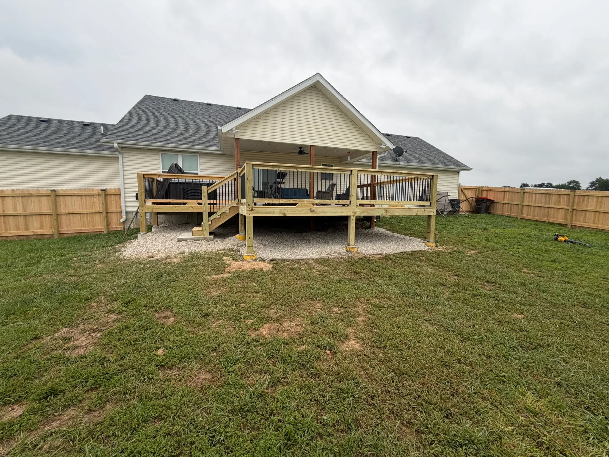 Finished wood deck addition with stairs beside a fenced backyard