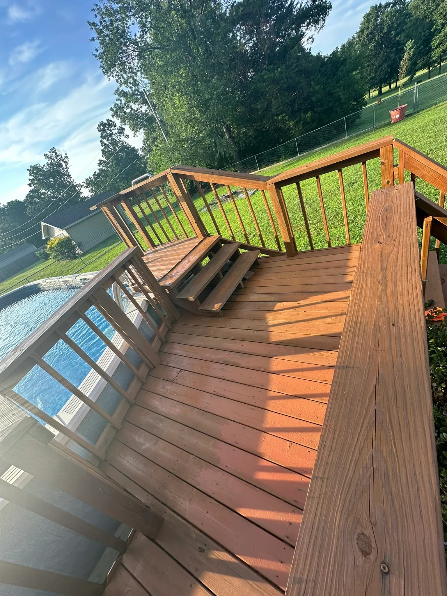 Elevated wood deck with stairs and railing beside a backyard pool