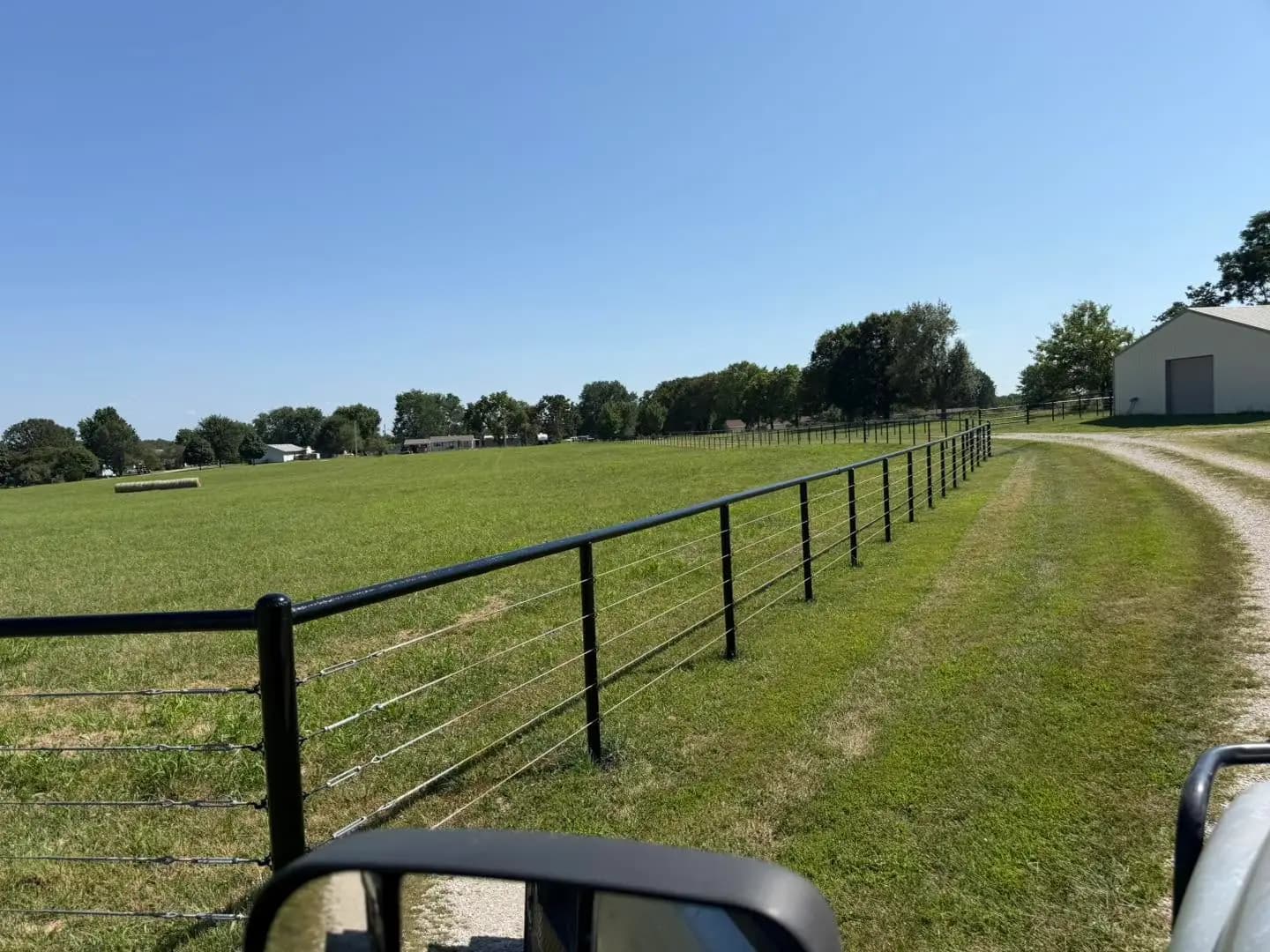 Black pipe fence running beside a mowed pasture lane