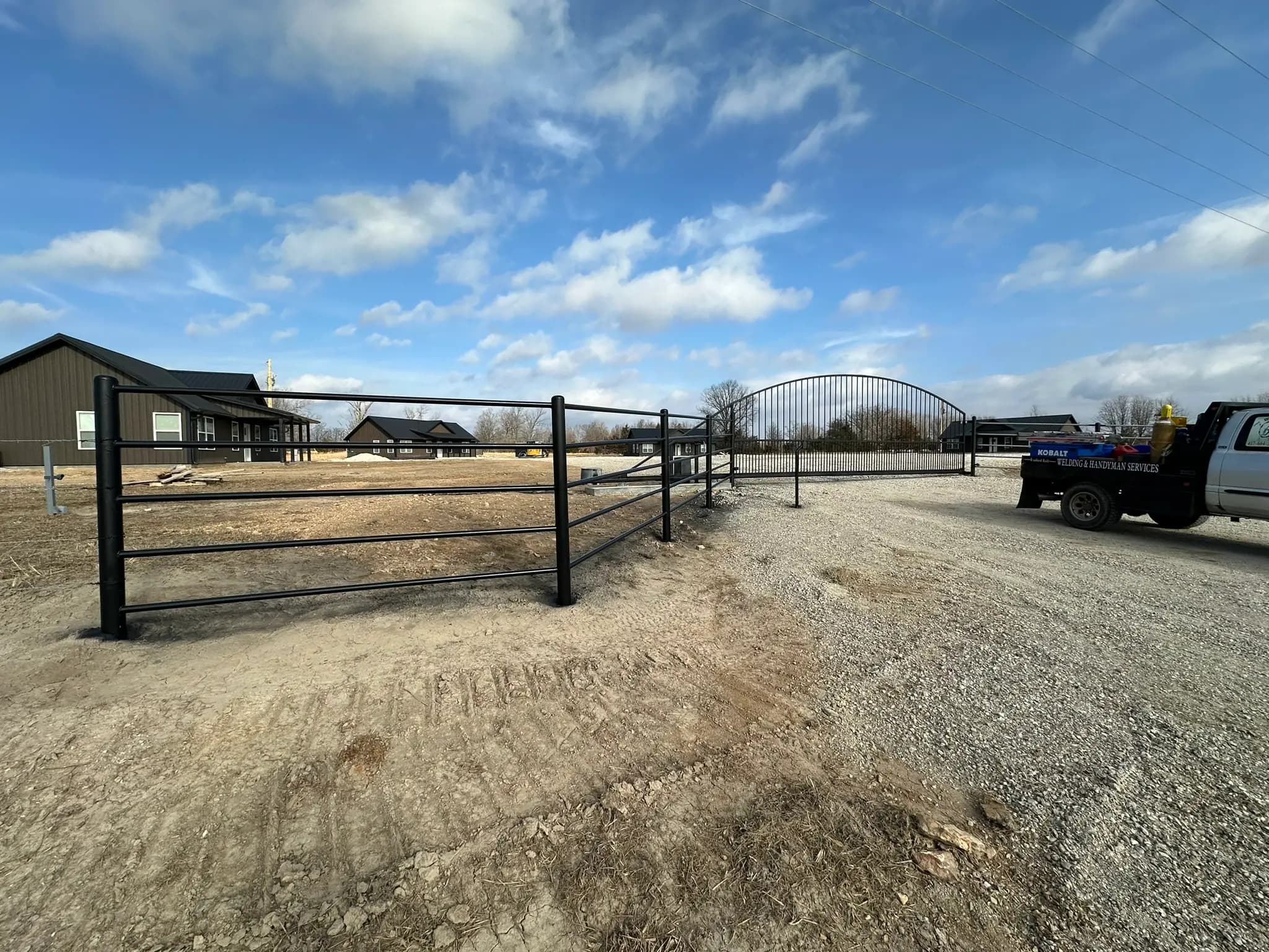 Black pipe fence and entrance gate along a gravel drive