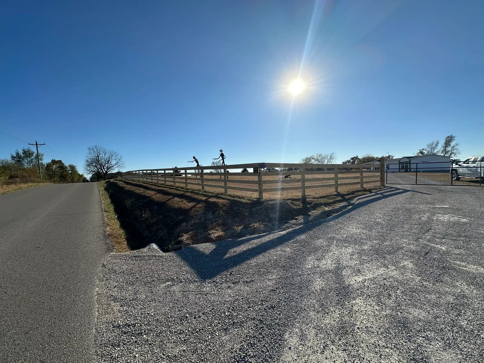 Continuous wood rail fence along a gravel driveway