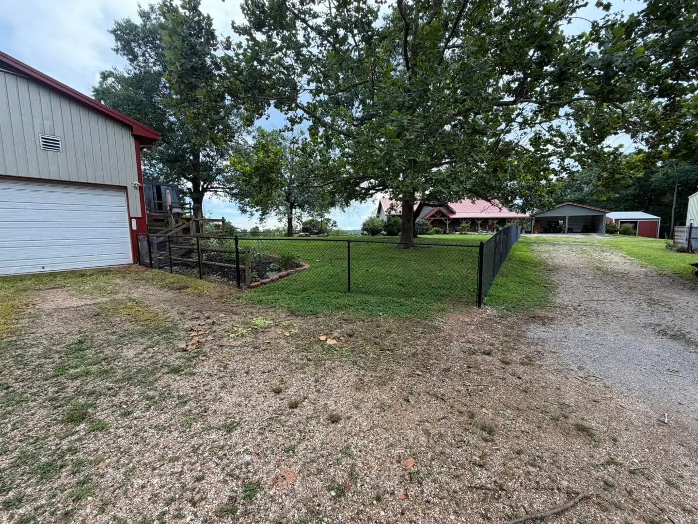 Black chain link fence beside a gravel drive and outbuilding