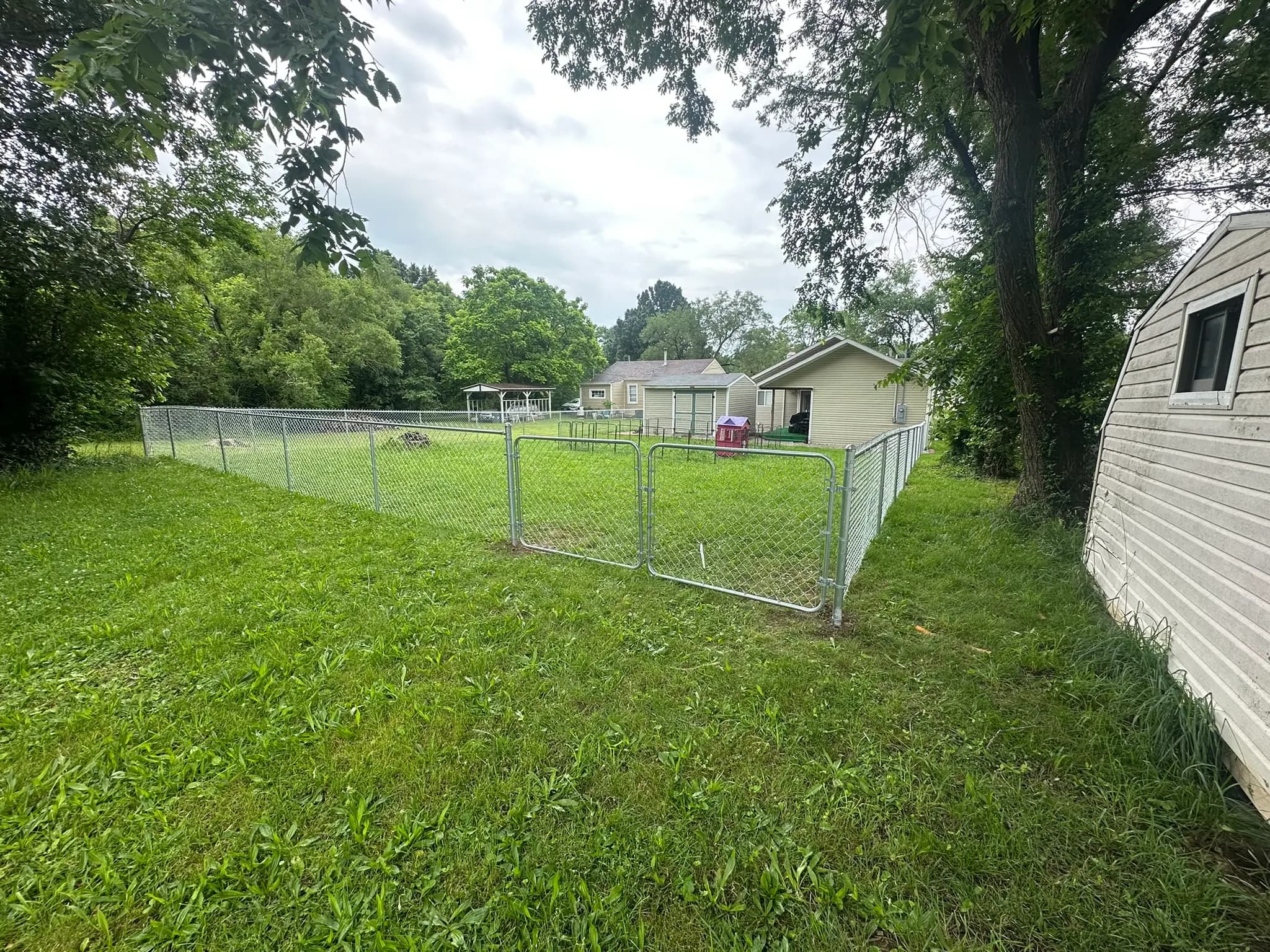 Chain link fence line beside a house and trees