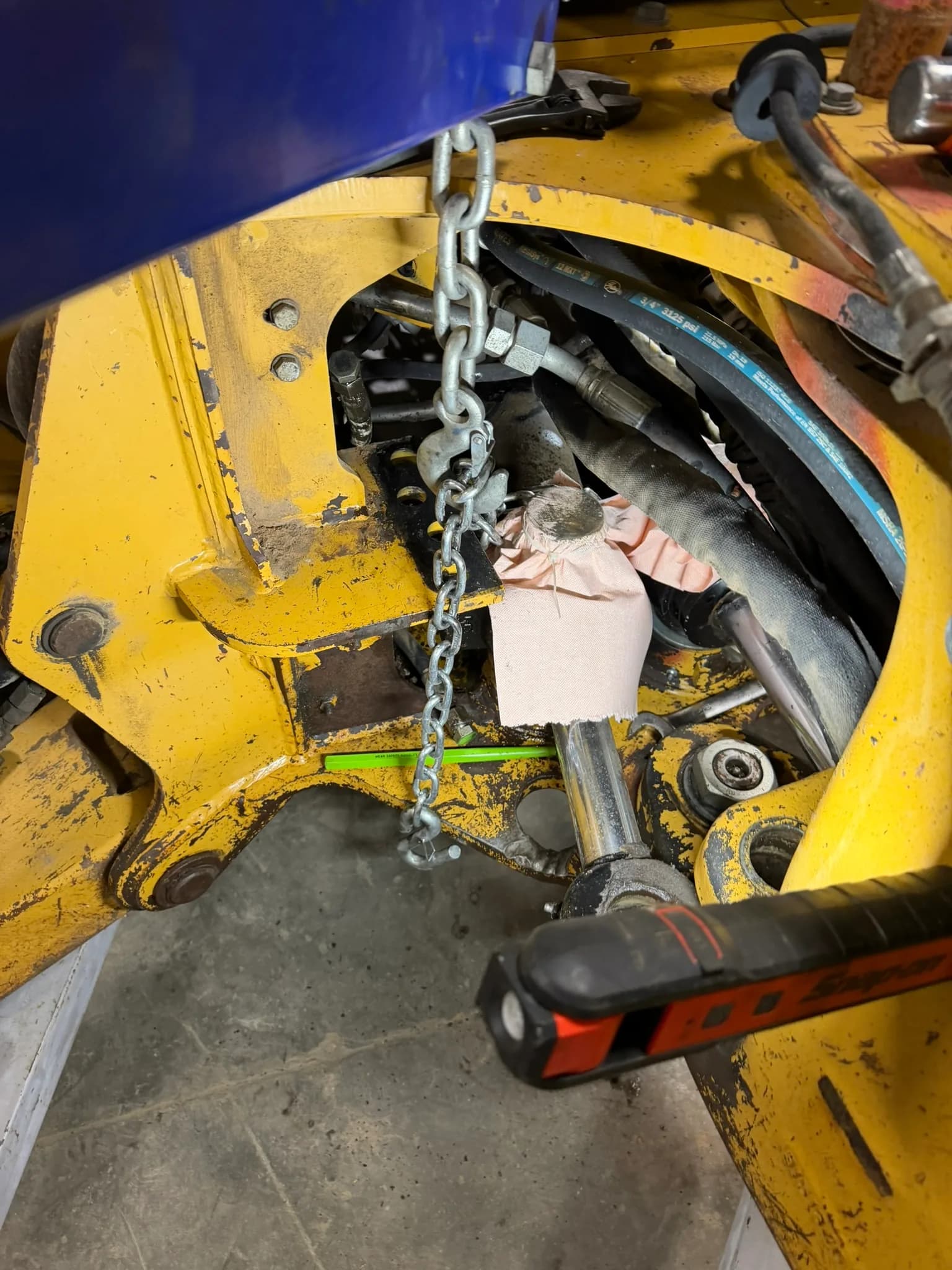 Close-up of a hydraulic cylinder repair with hoses and lifting chain