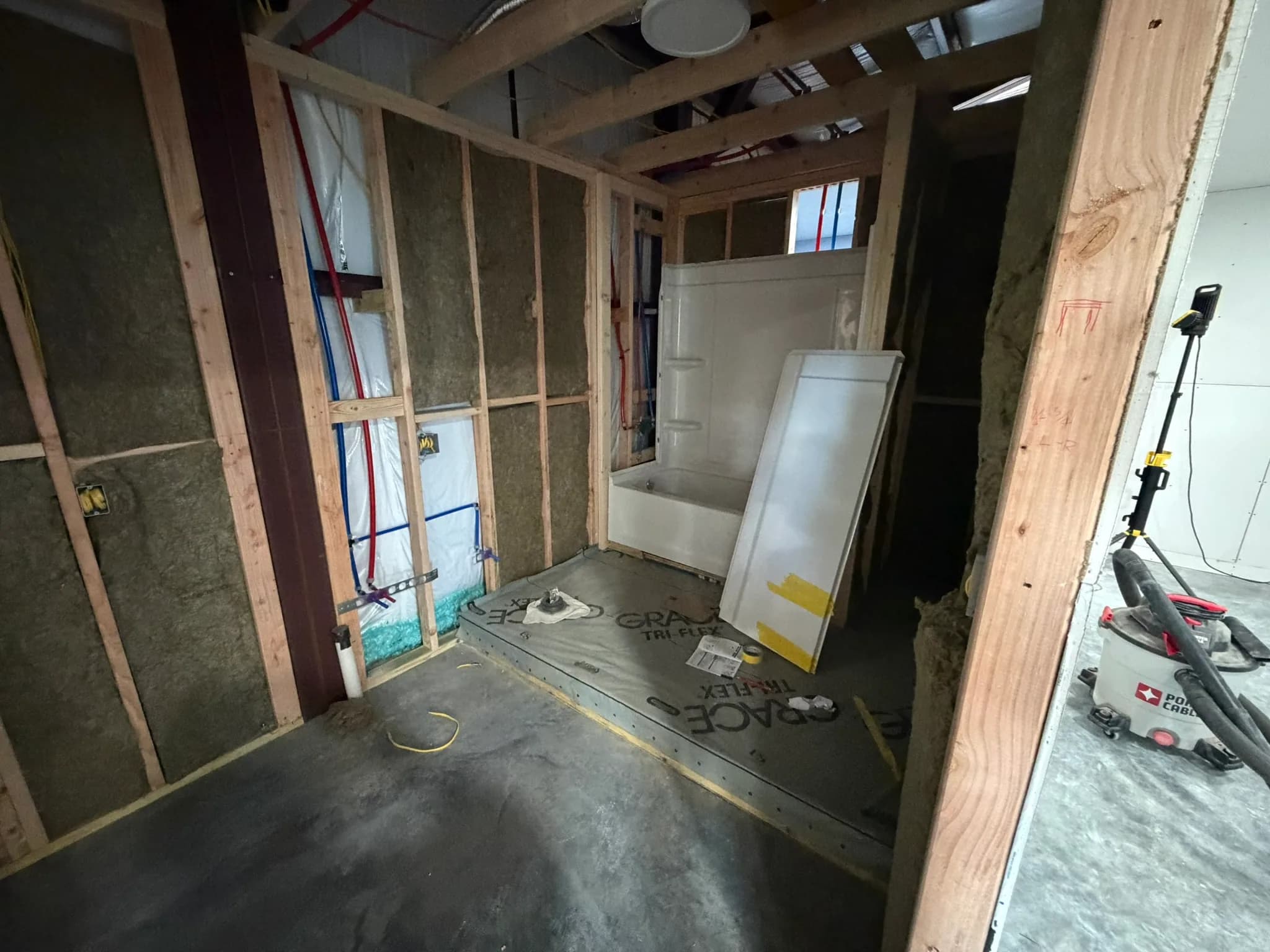 Bathroom remodel framing with shower base, plumbing, and insulation in progress