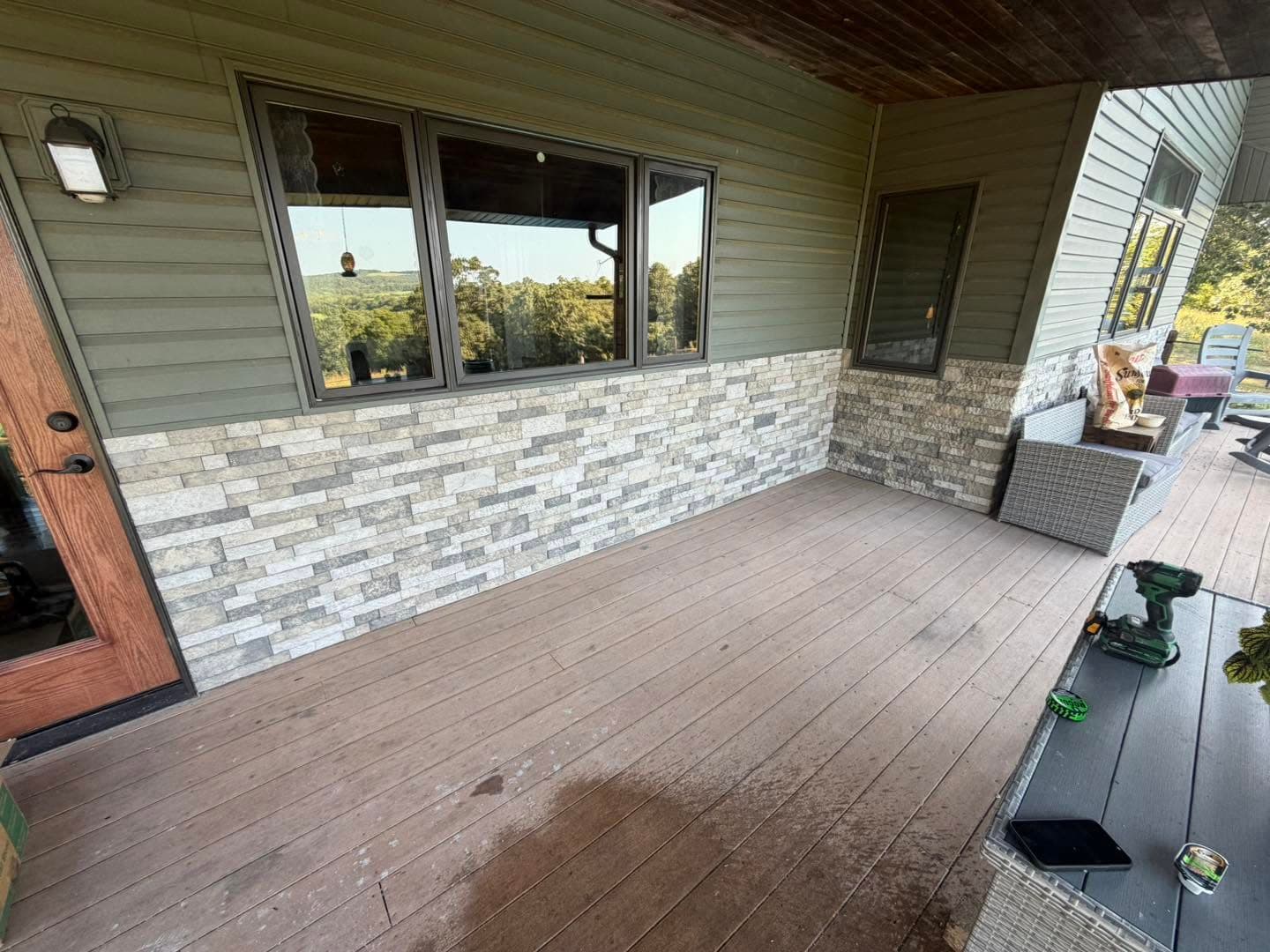 Long covered porch wall with completed stone-look brick wainscot below green siding