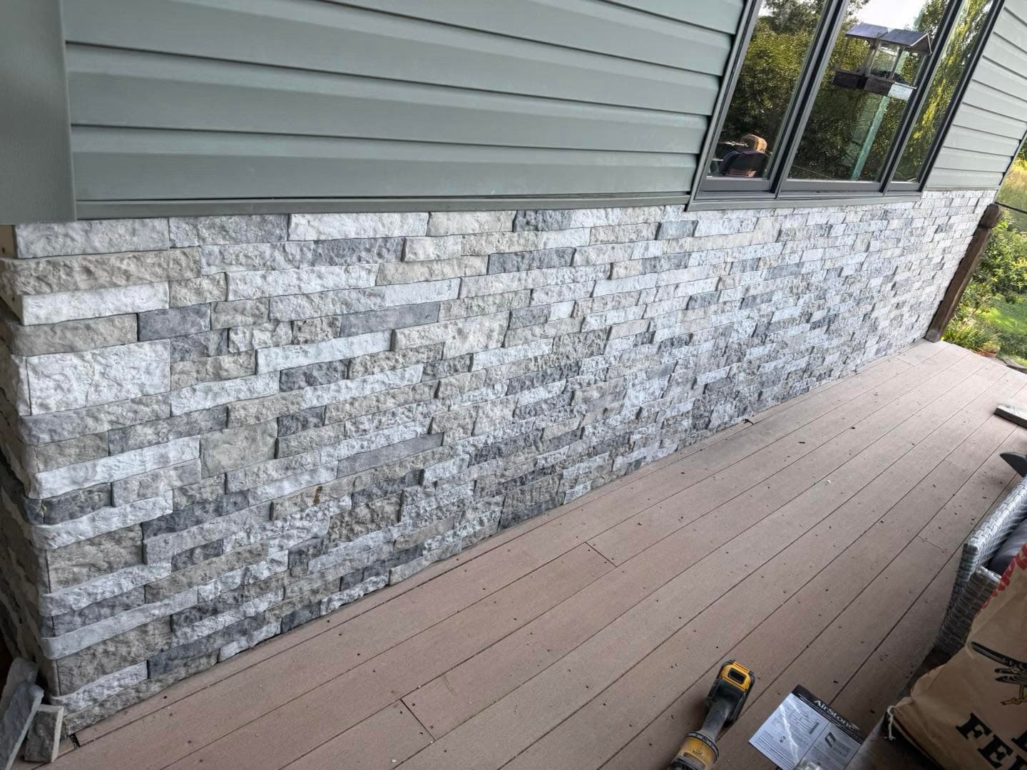 Close-up of textured gray brick wainscot installed below windows on a covered deck