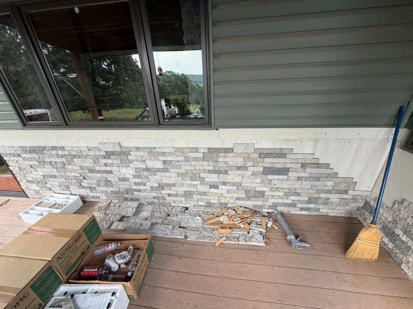 Brick wainscot installation in progress with stacked stone veneer set below the windows