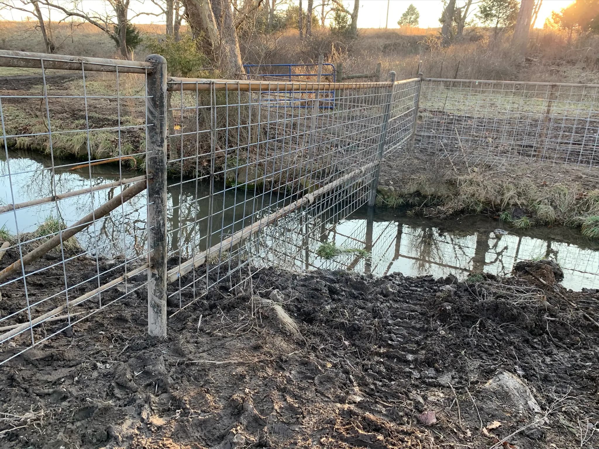 Wire and pipe fence repair near a muddy creek crossing